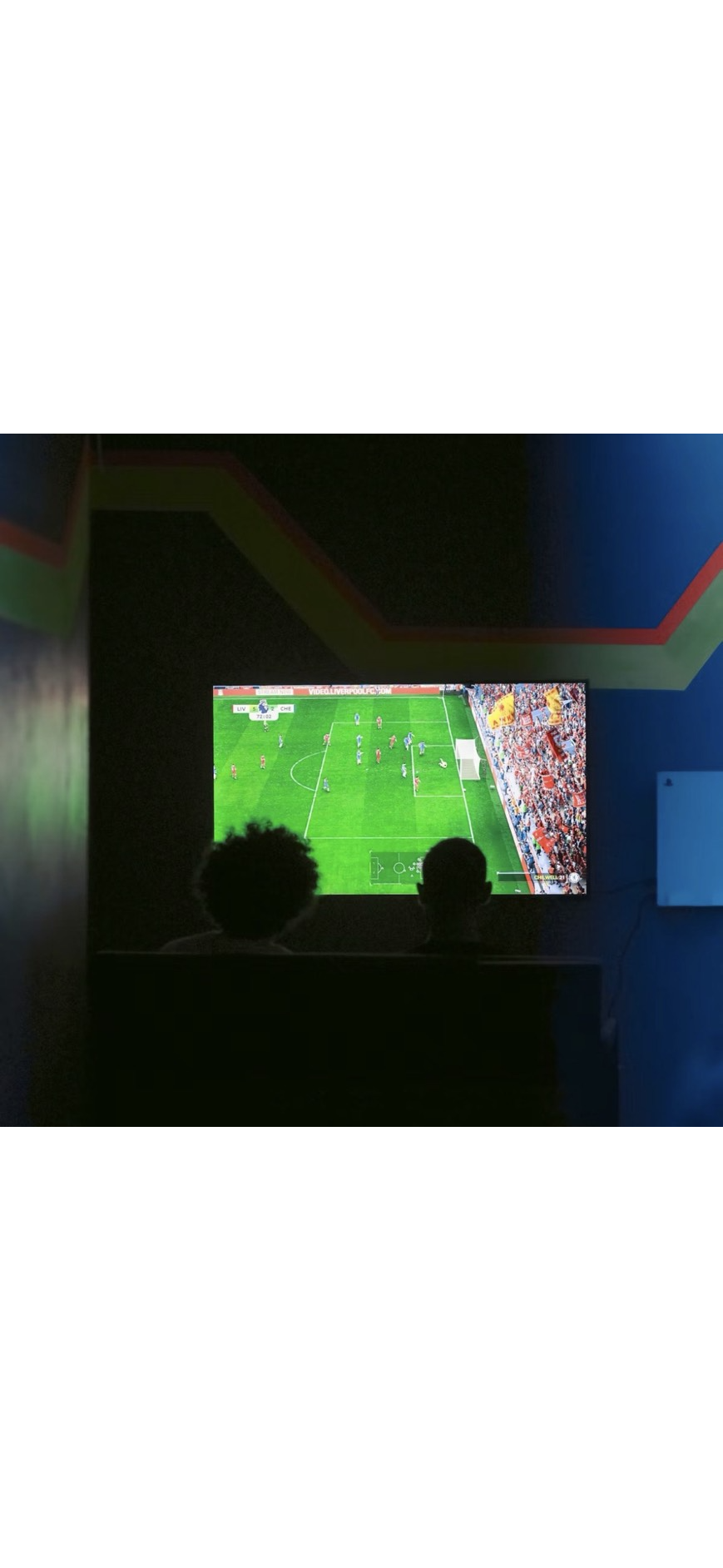 大きな画面でサッカーゲームを楽しむ二人の後ろ姿